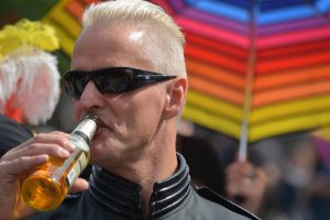 man met zonnebril en flesje bier voor regenboogkleuren parasol