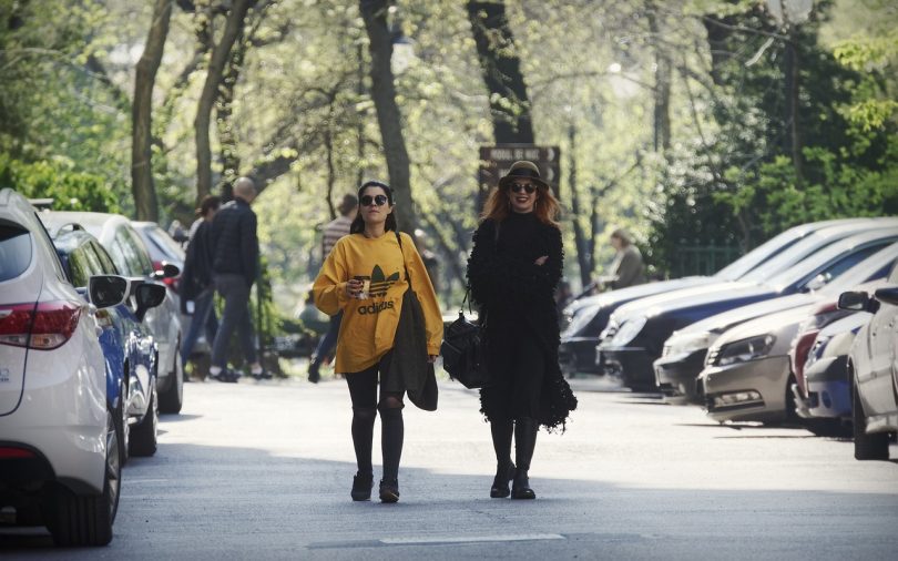 dames lopen tussen geparkeerde auto's door