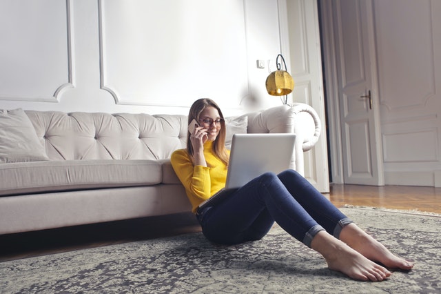 vrouw zit met laptop tegen zitbank